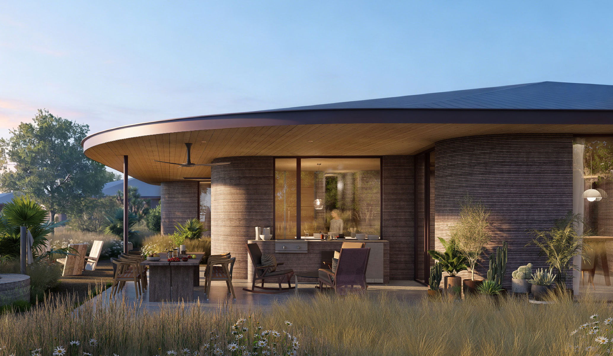 The outdoor kitchen and dining terrace of an ICON home under its broad curved roof, lounge chairs on the deck beyond and prairie grasses in the foreground